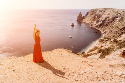 Woman red dress sea. Female dancer in a long red dress posing on a beach with rocks on sunny day. Girl on the nature on blue sky background