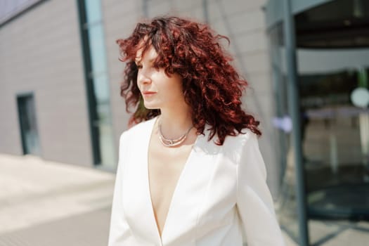 Portrait of a woman standing near a supermarket building. Caucasian model with long dark hair, wearing a white jacket and colored trousers