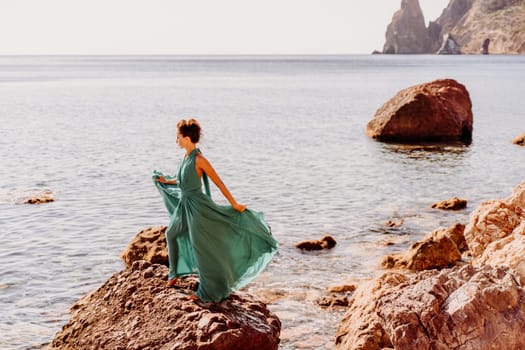 Woman green dress sea. Woman in a long mint dress posing on a beach with rocks on sunny day. Girl on the nature on blue sky background