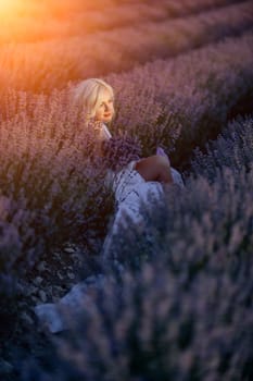 Blonde woman poses in lavender field at sunset. Happy woman in white dress holds lavender bouquet. Aromatherapy concept, lavender oil, photo session in lavender.