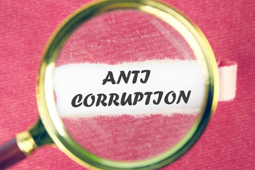 ANTI CORRUPTION text through a magnifying glass under a torn piece of red paper