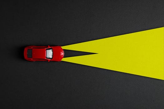 Top view of red toy car and yellow headlights on dark gray background