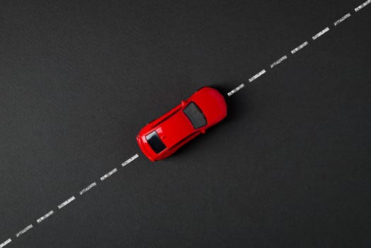 Top view of a red toy car driving on the drawn road line on a gray background