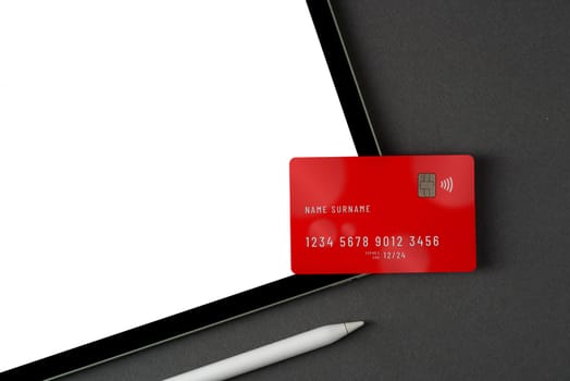 Credit card lying on tablet with blank screen on dark gray table