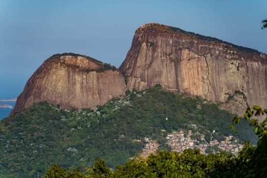 Adventurers summit Rio's Two Brothers rock with Rocinha favela at its base, showcasing a stark urban-nature contrast.
