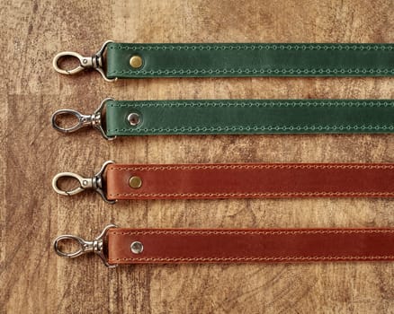 Collection of leather bag straps of different colors with metallic carabiners against wooden background, showcasing utility and craftsmanship