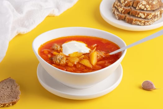 Ukrainian and Russian cuisine. Red borscht. Soup of tomatoes, cabbage and vegetables. Borscht in a white bowl on a yellow background.