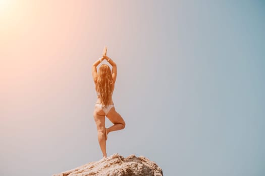 Woman meditating in yoga pose silhouette at the ocean, beach and rock mountains. Motivation and inspirational fit and exercising. Healthy lifestyle outdoors in nature, fitness concept.