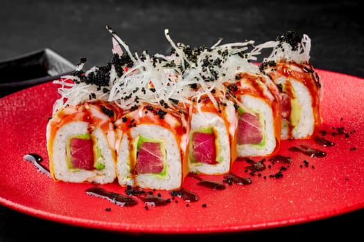 Sushi rolls with fresh tuna and avocado, topped with salmon and crab garnished with black masago roe and shredded daikon, served on bold red plate. Japanese food concept