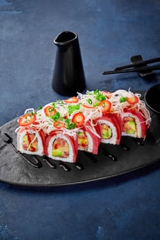 Appetizing Japanese sushi rolls topped with tuna, avocado, daikon, and chili slices, traditionally served with soy sauce on slate plate. Authentic cuisine
