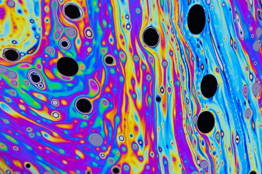 Bright green, pink, purple, blue and orange pastel colours swirl around intense black and white dots patterns on the surface of a soap bubble.
