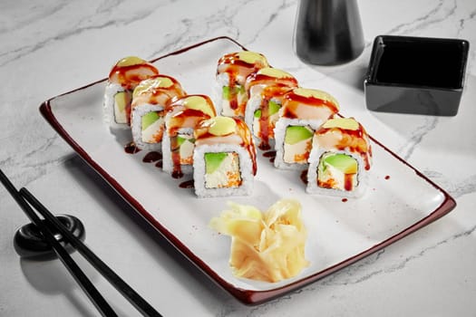 Appetizing sushi rolls with sea scallop, cream cheese, masago roe and avocado seasoned with spicy mayo an unagi sauce traditionally served with pickled ginger and soy sauce on plate