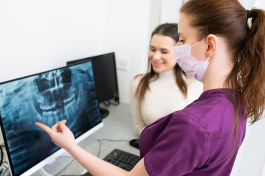 Female dentist shows the patient x-ray and discusses the concept of treatment in the clinic