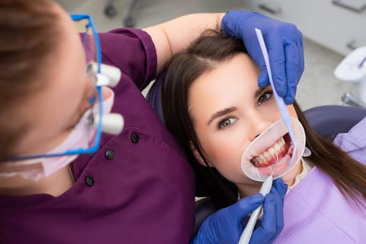 Woman patient undergoes regular dental checkup in hospital. Proficient dentist in mask checks strength of upper teeth with dental tools at appointment