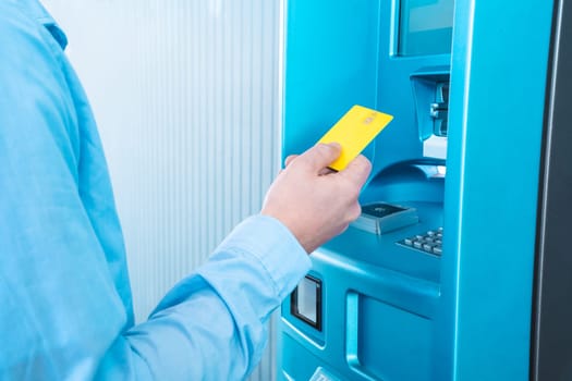 A man is inserting a blue credit card into a plastic ATM machine in a room filled with electric blue paint and fluid plastic bottles