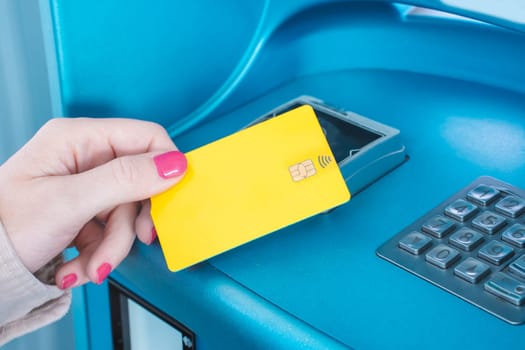 A woman is inserting a plastic yellow credit card into a blue ATM machine, featuring an electric blue computer keyboard as an input device, using her finger