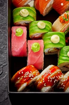 Colorful set of various Japanese rolls with tuna, salmon, eel, avocado and masago roe topped with spicy mayo, wasabi, packed in cardboard box, top view. Sushi delivery concept