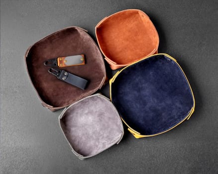 Folding colorful leather valet trays of different sizes decorated with embossed suede interior for keeping keys or small change arranged on gray background, top view. Handmade genuine leather products