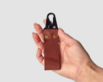 Female hand presenting sturdy handcrafted brown leather keychain engraved with DAD with black durable metal carabiner clasp and rivets against white background. Concept of thoughtful personalized gift