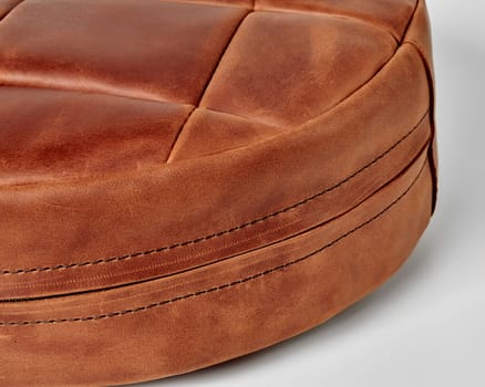 Close-up detailed view of brown leather patchwork floor cushion with neat stitching lines and hidden side zipper on white background. Artisanal interior design item
