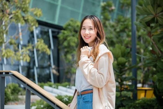 A city portrait of a cheerful Asian woman holding headphones embodies the modern joys of music communication and carefree happiness.