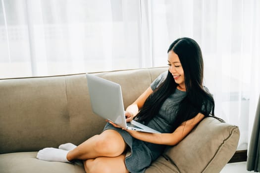 Happy woman on sofa uses laptop for ecommerce watching videos learning. Embracing success studying and relaxation at home. Modern technology for education and shopping.