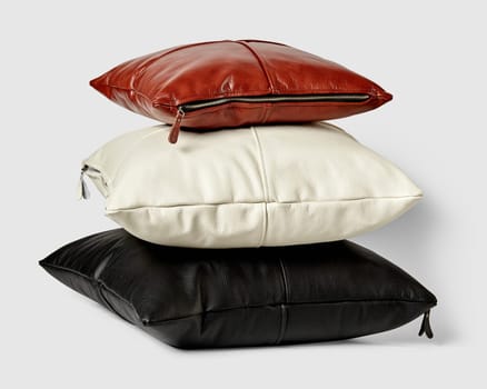 Stack of stylish minimalist square pillows of different sizes in black, white, and brown genuine leather with visible side zippers on light background. Handmade interior accessories