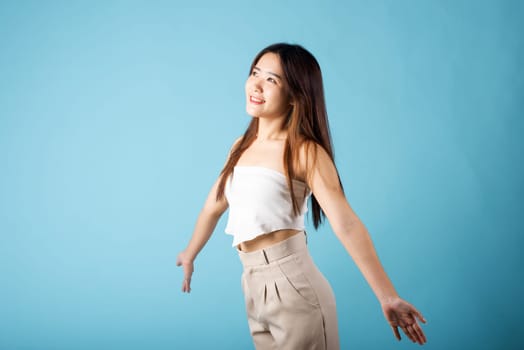 Asian young woman arms open to sunlight studio shot isolated on blue background, happy female smiling alone freedom carefree, welcome
