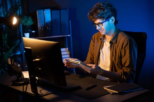 Young Businessman looking on notebook for new startup project job at neon light modern office surround by desk. Writing on marketing network online planning on market channel design concept. Gusher.