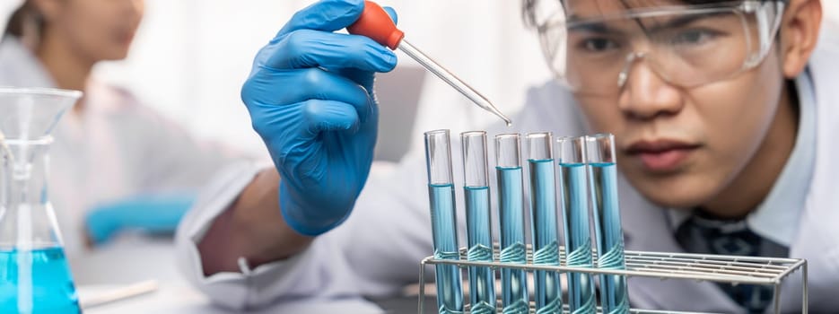 Group of dedicated scientist conduct chemical experiment in medical laboratory, carefully drop precise amount of liquid from pipette into test tube for vaccine drug or antibiotic development. Neoteric