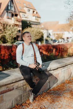 Man Sitting on Stairs in Old European City And Holding Photo Camera. Contemporary Stylish Blogger And Photographer