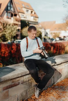 Man Sitting on Stairs in Old European City And Holding Photo Camera. Contemporary Stylish Blogger And Photographer