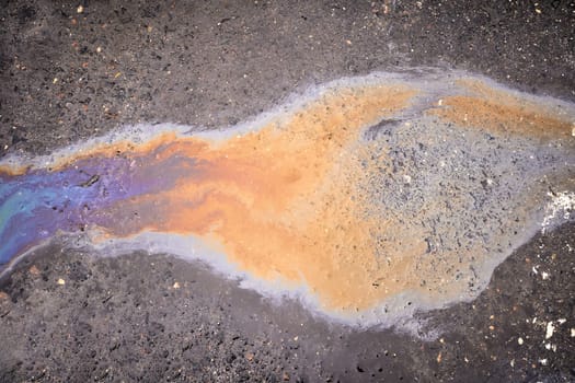 Background of a puddle of gasoline spilled on the road. Gasoline leak. A colorful stain of engine oil on the road