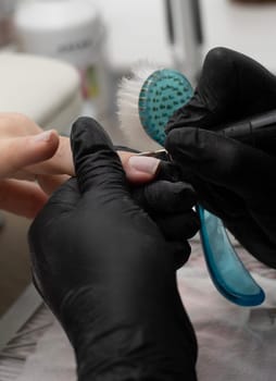 Beauty concept. A manicurist in black latex gloves makes a hygienic hardware manicure with a Fraser to a client in a beauty salon. Close-up. Vertical.