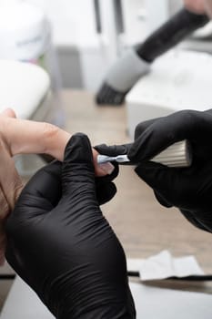 Beauty concept. A manicurist in black latex gloves makes a hygienic manicure and paints the client's nails with gel polish in a beauty salon. Close-up. Vertical.