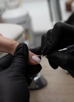 Beauty concept. A manicurist in black latex gloves makes a hygienic manicure and paints the client's nails with gel polish in a beauty salon. Close-up. Vertical.