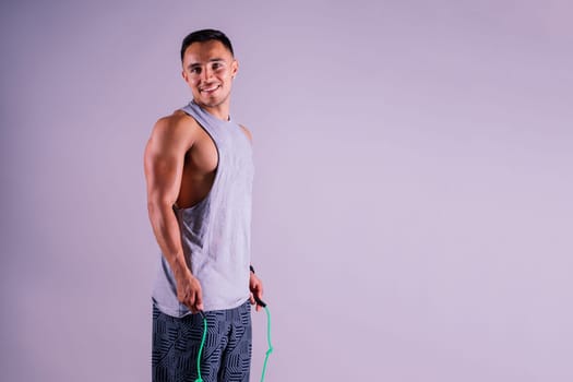 Young man exercising with skipping rope and looking at the camera isolated on grey background