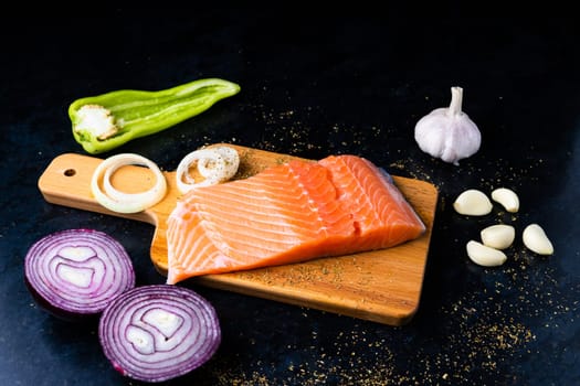 Raw salmon filet with rosemary and spices on a plate, black stone background. Top view, flat lay