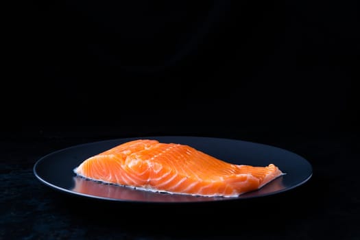 Raw salmon filet with rosemary and spices on a plate, black stone background. Top view, flat lay