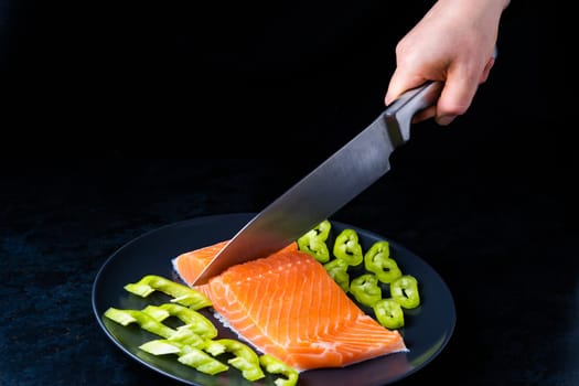 Raw salmon filet with rosemary and spices on a plate, black stone background. Top view, flat lay