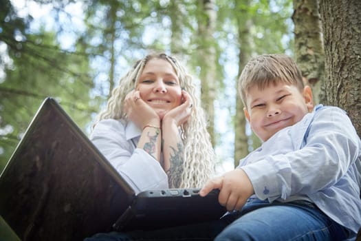 Kirov, Russia - June 12, 2023: Son with laptops in forest And Mom is proud of him. Fat young clever teenage boy with modern IT technologies in nature