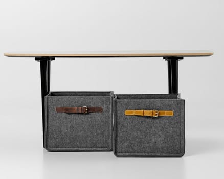 Functional and fashionable grey felt organizers with distinctive leather straps, placed under office desk for tidy workspace. Artisanal interior accessories