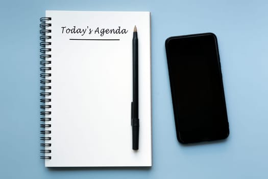 TODAY'S AGENDA written on notebook with pen and smartphone on blue background. Business concept.