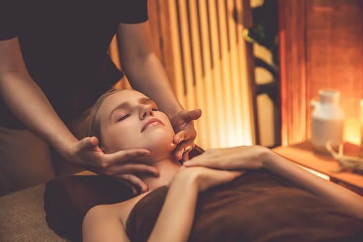 Caucasian woman enjoying relaxing anti-stress head massage and pampering facial beauty skin recreation leisure in warm candle lighting ambient salon spa in luxury resort or hotel. Quiescent