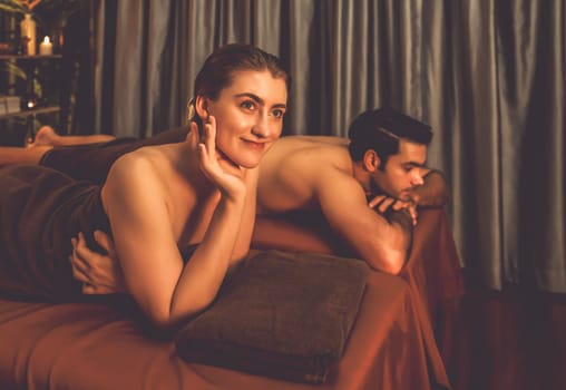 Caucasian couple customer enjoying relaxing anti-stress spa massage and pampering with beauty skin recreation leisure in warm candle lighting ambient salon spa at luxury resort or hotel. Quiescent