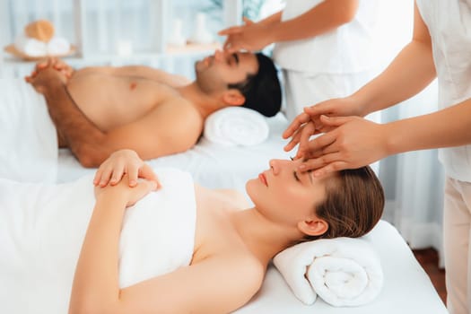 Caucasian couple enjoying relaxing anti-stress head massage and pampering facial beauty skin recreation leisure in dayspa modern light ambient at luxury resort or hotel spa salon. Quiescent