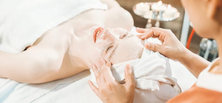 Portrait of beautiful caucasian woman having facial massage with homemade facial mask while lies on spa bed surrounded by beauty electrical equipment and peaceful nature environment. Tranquility.