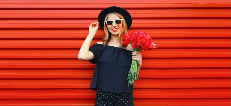 Portrait of beautiful happy smiling woman with bouquet of red rose flowers in black round hat
