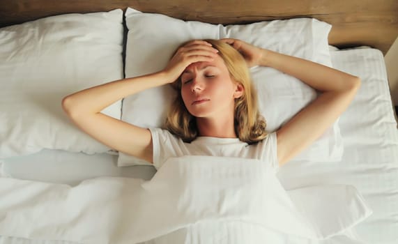Upset exhausted woman with headache, pain tension in the head, suffers from migraine lying on the bed on pillow in bedroom at home