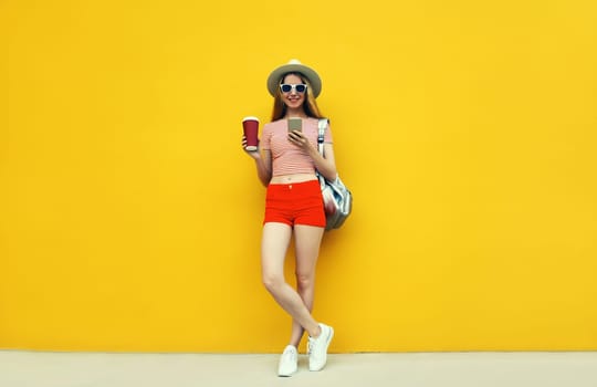 Summer image of traveler young woman 20s full length with mobile phone looking at device in casual straw hat with backpack on bright yellow background
